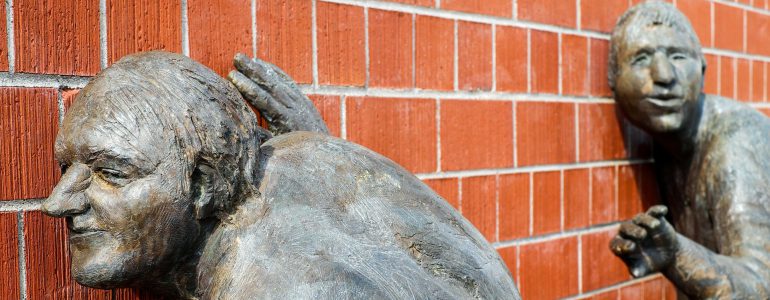 sculptured men listening to a brick wall